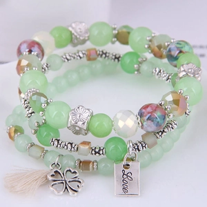 Close-up of triple-layered green bead bracelet with clover charm and Love metal tag