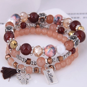 Detailed macro view of layered beaded bracelet with clover charm and Love metal tag