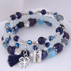 Close-up of three-layered blue beaded bracelets with silver clover and tassel charms