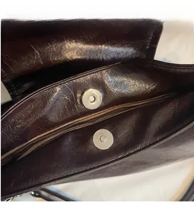 Detail view of silver magnetic buckles and oily leather texture on brown handbag