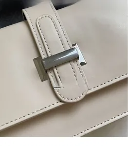 Close-up of cream leather shoulder bag featuring a rectangular metal buckle and fine stitching