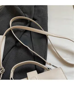 Detail of smooth beige leather long strap with silver metal hooks on a square bag