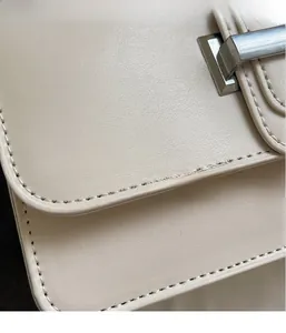 Detailed macro view of the creamy white textured leather flap and silver metal buckle