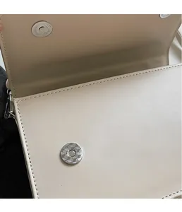 Detail of premium geometric engraved magnetic clasp on a beige leather crossbody bag