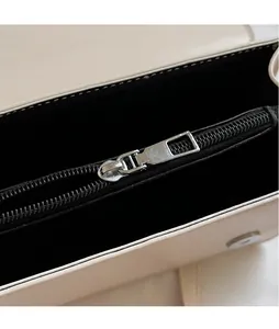 Detail view of the sleek silver zipper and black interior lining of this cream square bag