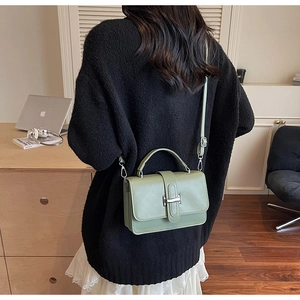 Detail of sage green rectangular crossbody bag with silver H-buckle in a cozy setting
