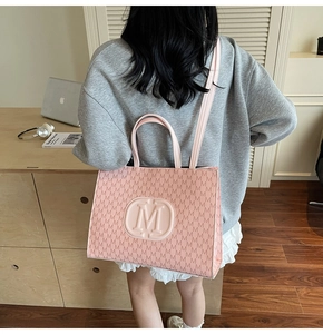 Close-up of pink tote bag with embossed M logo and monogram pattern in office setting
