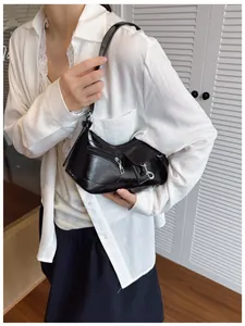 Gros plan d'un sac à bandoulière noir brillant asymétrique avec zips métalliques