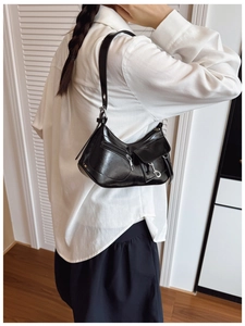 Fashionable black glossy underarm bag with silver zippers shown on shoulder in macro detail
