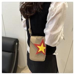 Detail of a beige mini crossbody bag with red and yellow star patches and golden hardware