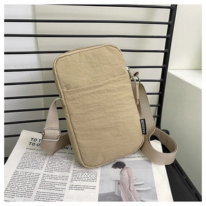 Detail of khaki nylon phone bag showing front pocket and woven fashion tag on metal grid