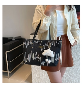 Close-up of black tote bag with white wave patterns and a plush cloud charm pendant
