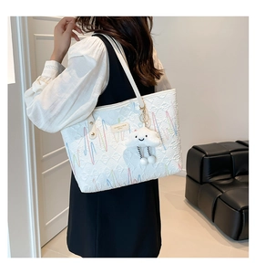 Detail of white tote bag featuring embroidered wave patterns and cloud plush charm