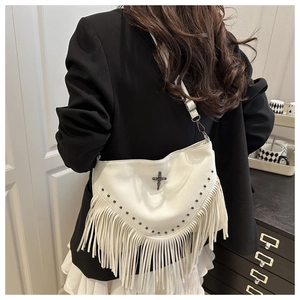 Détail d'un sac bandoulière blanc à franges avec rivets métalliques et pompons bohèmes