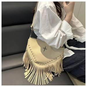 Détail du sac punk beige avec croix argentée, clous métalliques et longues franges