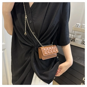 Detail of a caramel quilted mini chain bag worn by a model in a stylish indoor setting