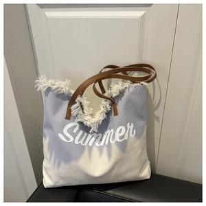 Detail of canvas beach tote with blue gradient tie-dye, fringe trim, and Summer print