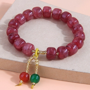 Bracelet à perles rouges à texture craquelée et pompon ethnique sur fond beige épuré