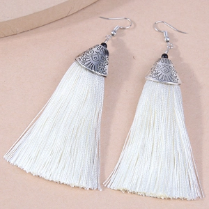 Macro shot of silver boho earrings featuring vintage relief caps and white silk tassels