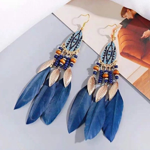 Detail of bohemian drop earrings featuring deep blue feathers and metal leaf charms