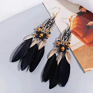 Bohemian vintage long earrings with black feathers and golden metal leaves on stylish background