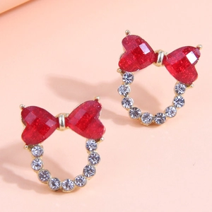 Détail de boucles d'oreilles nœuds dorées avec cristaux de cœur rouges et strass brillants
