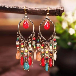 Orecchini pendenti boho con perline colorate e nappe metalliche su sfondo naturale