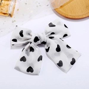 Elegant white chiffon hair bow clip with black heart print on a wooden tray