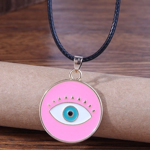 Pink evil eye pendant necklace with gold accents and black braided wax cord on wood