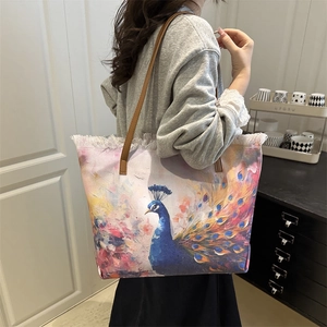 Large canvas tote bag with peacock print and brown leather straps in a lifestyle setting