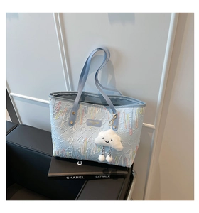 Detail of light blue tote bag featuring wavy colorful embroidery and cloud plush charm