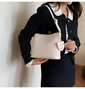 Close-up of cream-colored litchi grain leather shoulder bag with embossed brand logo