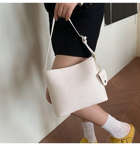 Detail of cream bucket bag with lychee grain texture and mini pouch charm on shoulder strap