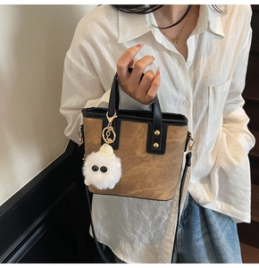 Detail of tan mini tote bag featuring gold lettering, black handles, and a cute plush toy