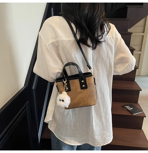 Brown textured bucket bag with white plush charm shown on model near stairs