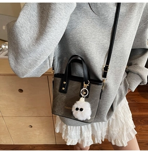 Detail of gray canvas mini tote bag with black leather trim and plush charm