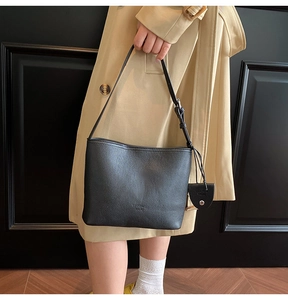 Close-up of black lychee-grain leather bucket bag with adjustable strap on a model