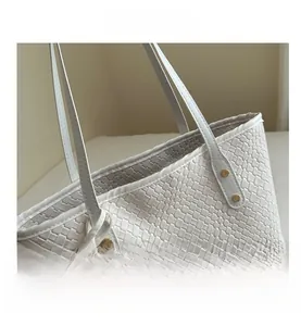 Close-up of white woven tote bag featuring golden rivet accents and fine stitching detail