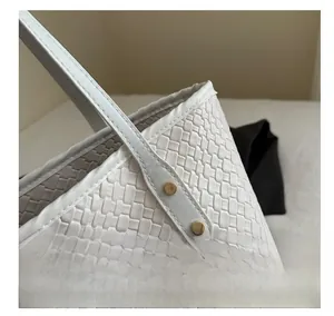 Detailed close-up of woven white leather texture with gold metal rivets on tote bag