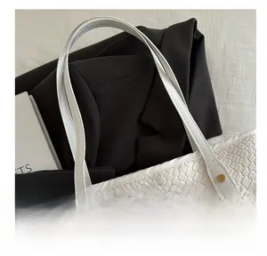 Detail of white woven tote bag featuring gold metal rivets and minimalist texture