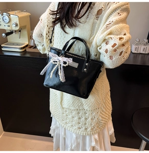 Detail van zwarte glanzende handtas met parelketting en witte kant strik decoratie