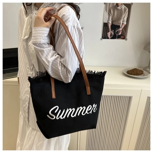 Détail du sac cabas en toile noire avec broderie Summer, bords frangés et anses en cuir