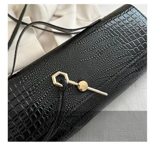 Detail of black faux leather bag with crocodile texture and gold hexagonal metal clasp