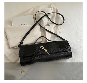 Close-up of black crocodile texture shoulder bag with gold key lock and slim strap