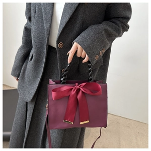 Détail du sac à main bordeaux avec grand nœud en soie et poignée noire torsadée chic