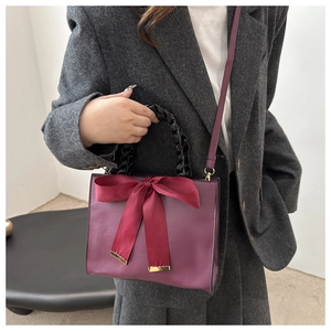 Detail of burgundy leather bag with a large satin bow and woven handle shown on model