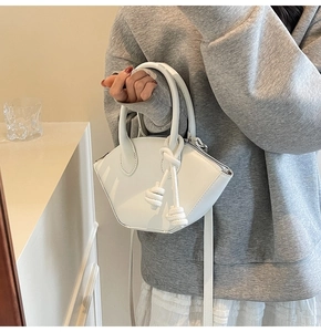 Détail du sac coquille blanc montrant la poignée à nœud élégante et la texture du cuir lisse