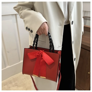 Detail of red leather handbag featuring oversized silk bow and black braided handle