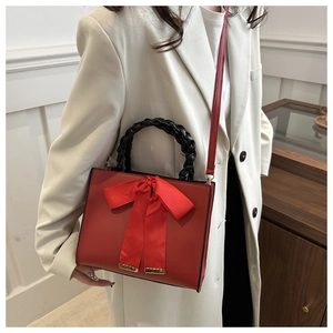 Detail of red bridal handbag with a large satin bow and black woven leather handle