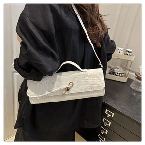 Detail of white crocodile embossed baguette bag with golden hardware and key charm
